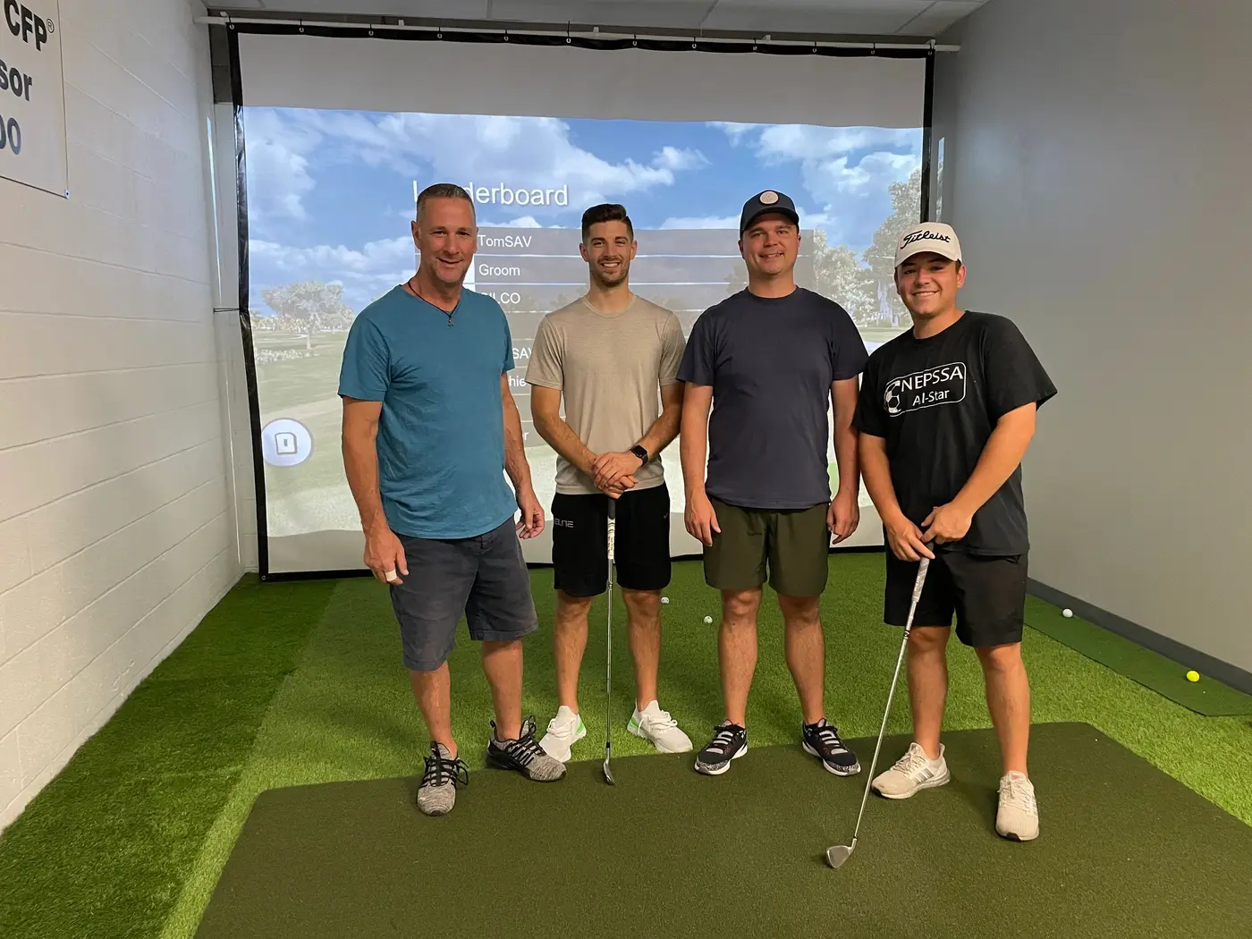Four golfers standing in the simulator bay in front of the screen
